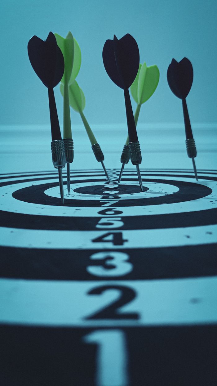 about-us-01 Close-up view of darts hitting a bullseye on a target board, symbolizing precision and focus.